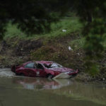 
              A damaged car sits in the water on Wednesday, Aug. 3, 2022, in Hindman, Ky., after massive flooding carried the car to the water. Temperatures are soaring in a region of eastern Kentucky where people are shoveling out the wreckage of massive flooding.  (AP Photo/Brynn Anderson)
            