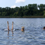 
              Anastasiia Aleksandrova, 12, left, plays in the water while swimming with her grandparents, Olena, and Andreii, right, at a lake in Sloviansk, Donetsk region, eastern Ukraine, Monday, Aug. 8, 2022. With cities largely emptied after hundreds of thousands have evacuated to safety, the young people that remain face alienation, loneliness and boredom as unlikely yet painful counterpoints to the fear and violence Moscow has unleashed on Ukraine. (AP Photo/David Goldman)
            