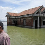 
              FILE - A man walks past a house abandoned after it was inundated by water due to the rising sea level in Sidogemah, Central Java, Indonesia, Nov. 8, 2021. Climate hazards such as flooding, heat waves and drought have worsened more than half of the hundreds of known infectious diseases in people, such as malaria, hantavirus, cholera and even anthrax, according to a new study released Monday, Aug. 8, 2022. (AP Photo/Dita Alangkara, File)
            