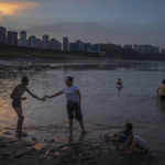 
              People swim in shallow water near the dry riverbed of the Yangtze River in southwestern China's Chongqing Municipality, Friday, Aug. 19, 2022. Ships crept down the middle of the Yangtze on Friday after the driest summer in six decades left one of the mightiest rivers shrunk to barely half its normal width and set off a scramble to contain damage to a weak economy in a politically sensitive year. (AP Photo/Mark Schiefelbein)
            
