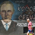 
              A man passes by graffiti depicting Russian President Vladimir Putin, reading: "Kosovo is Serbia" in Belgrade, Serbia, Monday, Aug. 1, 2022. Kosovo's authorities early Monday moved to ease mounting ethnic tensions in the country by delaying a controversial order on vehicle license plates and identity cards that triggered riots by minority Serbs who put up roadblocks, sounded air raid sirens and fired their guns into the air. (AP Photo/Darko Vojinovic)
            