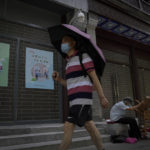 
              A man wearing a face mask and holding an umbrella to shield from the sunlight as he walks by an elderly man collecting recycle items in front of vacant shop lots at Qianmen Street in Beijing, Wednesday, Aug. 17, 2022. Factories in China's southwest have shut down after reservoirs used to generate hydropower ran low in a worsening drought, adding to economic strains at a time when President Xi Jinping is trying to extend his position in power. (AP Photo/Andy Wong)
            