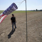 
              Hay farmer Milan Adams stands in a dry hay field near a wind sock, left, in Exeter, R.I., Tuesday, Aug. 9, 2022. Adams said in prior years it rained in the spring. This year, he said, the dryness started in March, and April was so dry he was nervous about his first cut of hay. (AP Photo/Steven Senne)
            