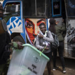 
              An electoral worker smiles as a policeman helps her to offload ballot boxes from a minibus transporting electoral workers to a collection and tallying center in Nairobi, Kenya Wednesday, Aug. 10, 2022. Kenyans are waiting for the results of a close but calm presidential election in which the turnout was lower than usual. (AP Photo/Ben Curtis)
            