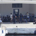 
              Migrants guarded by coast guard, sit in Kapsali port on the southern island of Kythera, Greece, on Wednesday, Aug. 17, 2022. A second boat carried the depicting migrants arrive on the island on Wednesday, after another sailboat ran aground in the early hours of the morning with 97 people on board. (Giorgos Samios/kythera.news via AP)
            