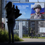 
              A woman uses her mobile phone as she walks past a billboard with a portrait of a Russian soldier and the words "Glory to the heroes of Russia" in St. Petersburg, Russia, Saturday, Aug. 20, 2022. Six months after Russia sent troops into Ukraine, there's little sign of the conflict on Moscow's streets and the capital's residents seem unconcerned about the economic and political sanctions by Western countries. (AP Photo/Dmitri Lovetsky)
            