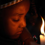 
              A child holds a candle during a baptism ceremony inside the chapel of the Kalunga quilombo during the culmination of the week-long pilgrimage and celebration for the patron saint "Nossa Senhora da Abadia" or Our Lady of Abadia, in the rural area of Cavalcante in Goias state, Brazil, late Monday, Aug. 15, 2022. (AP Photo/Eraldo Peres)
            