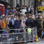 
              People wait ahead of the Queens cortege which carries the coffin of Queen Elizabeth II, along the Royal Mile in Edinburgh, Scotland, Sunday, Sept. 11, 2022. The coffin of the late Queen Elizabeth II is being transported Sunday on a journey from Balmoral to the Palace of Holyroodhouse in Edinburgh, where it will lie at rest before being moved to London later in the week. (AP Photo/Jon Super)
            
