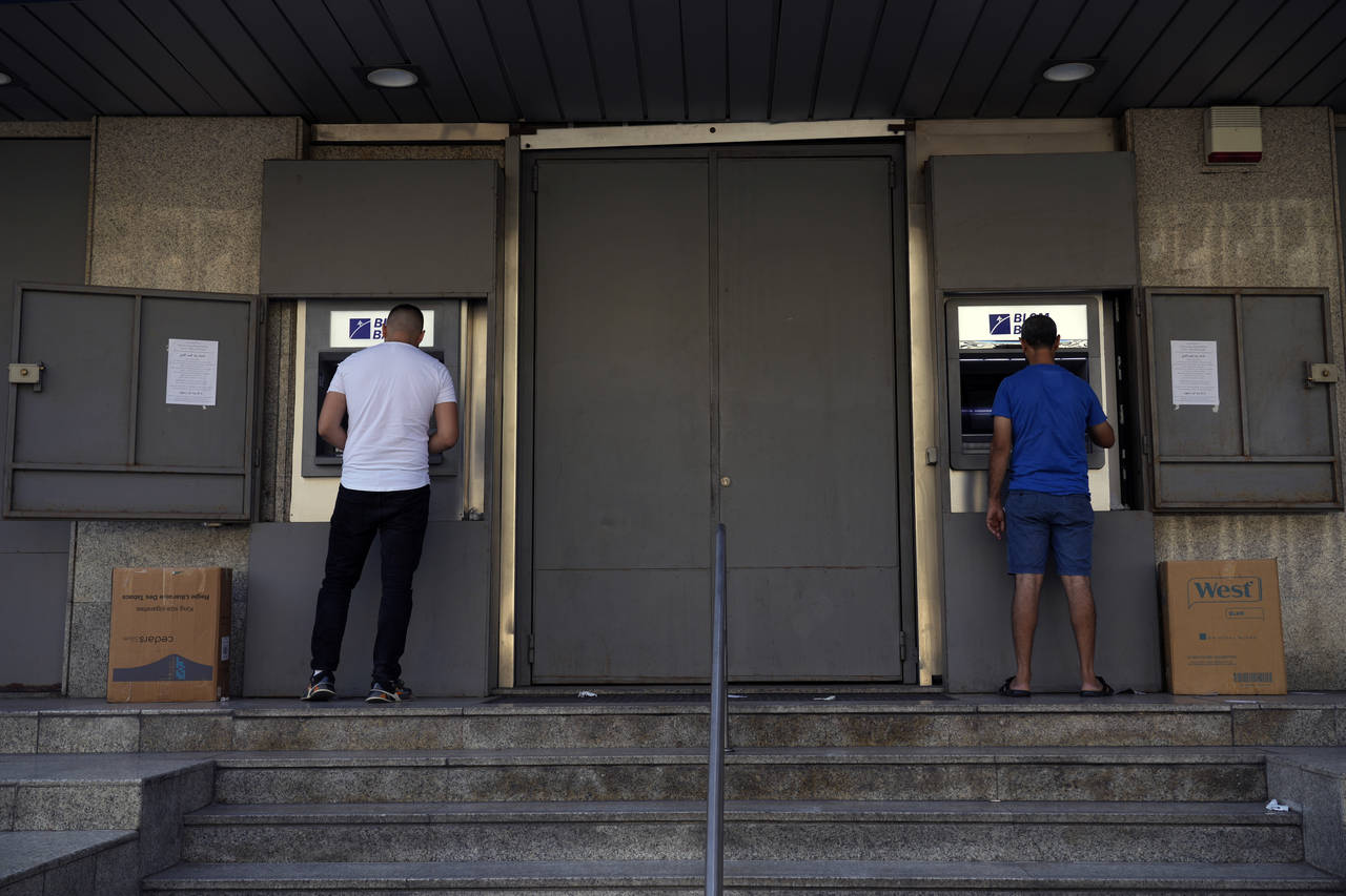 People use an ATM outside a closed Blom Bank branch that is covered with metal sheets to prevent va...