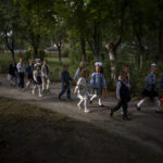 
              Students walk together entering in their class during their first day of school at a public school in Irpin, Ukraine, Thursday, Sept. 1, 2022. Ukrainian children return to school without sharing memories from their holidays. They share stories of how they survived the first months of the war. For many children, last semester finished the day before Russia invaded Ukraine on the 24th of February. The ongoing war remains the biggest challenge for the educational system of Ukraine. (AP Photo/Emilio Morenatti)
            
