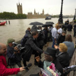 
              People are interviewed by TV reporters as they wait opposite the Palace of Westminster to be first in line bidding farewell to Queen Elizabeth II in London, Tuesday, Sept. 13, 2022. Queen Elizabeth II, Britain's longest reigning monarch, will be lying in state at Westminster Palace from Wednesday. ( (AP Photo/Markus Schreiber)
            