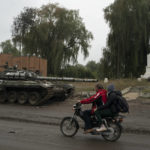 
              People drive a motorcycle past blown Russian tank, with the letter Z on it, which has become the Russian emblem for the war on the road in the recaptured area of Izium, Ukraine, Wednesday, Sept. 14, 2022. (AP Photo/Leo Correa)
            