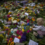 
              A child touches flowers left for Queen Elizabeth II at the Green Park memorial, near Buckingham Palace, in London, Sept. 10, 2022. (AP Photo/Emilio Morenatti)
            
