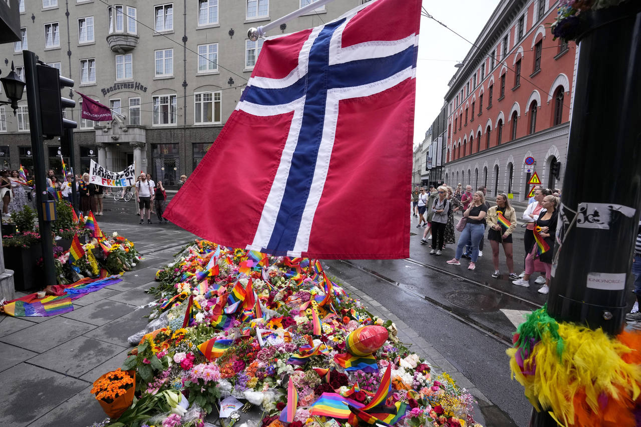 FILE - A Norwegian national flag flutters over flowers and rainbow flags that are placed at the sce...