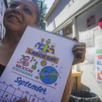 
              Marina Cortes, manager of the La Bonbonniere diner, shows off a calendar created by brothers Miguel and Carlos Cevallos, along with service posters commisioned for the diner, Tuesday, Aug. 30, 2022, in New York. For years the Cevallos brothers made a living drawing posters for nightclubs, taco trucks and restaurants, attracting clients by word of mouth, but an Instagram account changed a lot of that. (AP Photo/Bebeto Matthews)
            