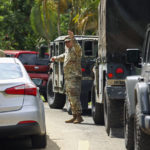 
              National Guards directs traffic on a road affected by Hurricane Fiona in Cayey, Puerto Rico, Tuesday, Sept. 20, 2022. Fiona triggered a blackout when it hit Puerto Rico’s southwest corner on Sunday. (AP Photo/Stephanie Rojas)
            