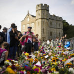 
              People gather at flowers and messages to tribute Queen Elizabeth II, in front of Windsor Castle in Windsor, England, Sunday, Sept. 11, 2022. Queen Elizabeth II, Britain's longest-reigning monarch and a rock of stability across much of a turbulent century, died Thursday Sept. 8, 2022, after 70 years on the throne. She was 96. (AP Photo/Markus Schreiber)
            