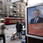 
              People pass by an election poster of Zeljko Komsic who is running for the Bosnian Presidency in the upcoming elections in Sarajevo, Bosnia, Tuesday, Sept. 27, 2022. Bosnia's upcoming general election could be about the fight against corruption and helping its ailing economy. But at the time when Russia has a strong incentive to reignite conflict in the small Balkan nation, the Oct 2. vote appears set to be an easy test for long-entrenched nationalists who have enriched cronies and ignored the needs of the people. (AP Photo/Armin Durgut)
            