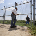
              Hugo Urbina, center, talks through his fence to migrants who crossed the Rio Grande illegally at his pecan farm, Heavenly Farms, Friday, Aug. 26, 2022, in Eagle Pass, Texas. The Texas National Guard and state troopers built a fence around Heavenly Farms and, in mid-August, locked a gate to arrest migrants after crossing the Rio Grande illegally. The Border Patrol felt the lock impeded operations and had it removed. (AP Photo/Eric Gay)
            