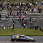
              Spectators watch as the cortege with the hearse carrying the coffin of Queen Elizabeth II drives on the M90 motorway as it makes its journey to Edinburgh from Balmoral in Scotland, Sunday, Sept. 11, 2022. The Queen's coffin is being transported Sunday on a journey from Balmoral to the Palace of Holyroodhouse in Edinburgh, where it will lie at rest before being moved to London later in the week. (AP Photo/Alastair Grant)
            