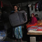 
              Climate refugee Jaidul Islam, left, holds up a large suitcase in which he carried some clothes for the kids, a mosquito net and two towels, when he left his flooded village with his family and migrated to this one room home in Bengaluru, India, Wednesday, July 20, 2022. (AP Photo/Aijaz Rahi)
            