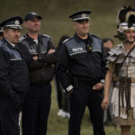
              Police officers watch reenactments of Roman Empire era gladiator fights standing next to a participant dressed as a Roman soldier in the village of Resca, Romania, Saturday, Sept. 3, 2022. (AP Photo/Vadim Ghirda)
            