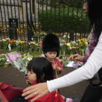 
              Sachiko Suckling with her 3 year-old twins, Naomi, left, and Louis, lay flowers outside Windsor Castle for late Queen Elizabeth II in Windsor, England, Thursday, Sept. 15, 2022. The Queen will lie in state in Westminster Hall for four full days before her funeral on Monday Sept. 19. (AP Photo/Gregorio Borgia)
            