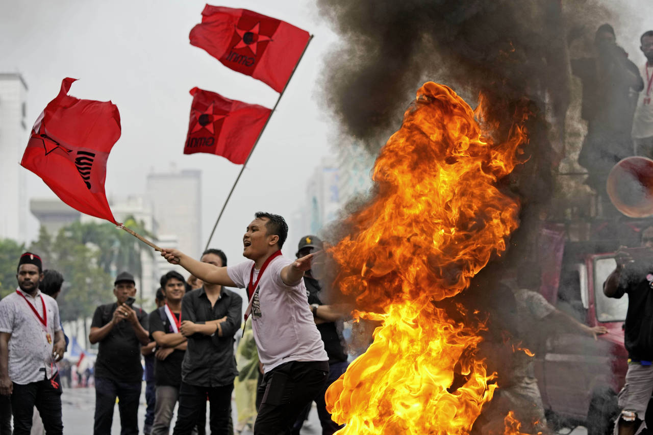 Student activists wave flags as they burn a tire during a rally against sharp increases in fuel pri...