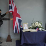 
              An embassy staff arranges the flag beside a picture of Queen Elizabeth II outside the British Embassy in Metro Manila, Philippines, Friday, Sept. 9, 2022. Queen Elizabeth II, Britain's longest-reigning monarch and a rock of stability across much of a turbulent century, died Thursday Sept. 8, 2022, after 70 years on the throne. She was 96. (AP Photo/Aaron Favila)
            