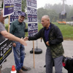 
              New Hampshire Republican U.S. Senate candidate Don Bolduc shakes hands with campaign volunteers while arriving with his dog "Victor" before voting, Tuesday, Sept. 13, 2022, in Stratham, N.H. (AP Photo/Charles Krupa)
            