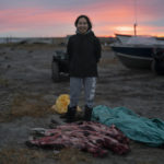 
              The setting sun colors the sky as Helen Kakoona, 28, stands for a photo with skinned seals in front of her in Shishmaref, Alaska, Monday, Oct. 3, 2022. "Home sweet home," Kakoona said of the village. "No other place feels like home but here." (AP Photo/Jae C. Hong)
            
