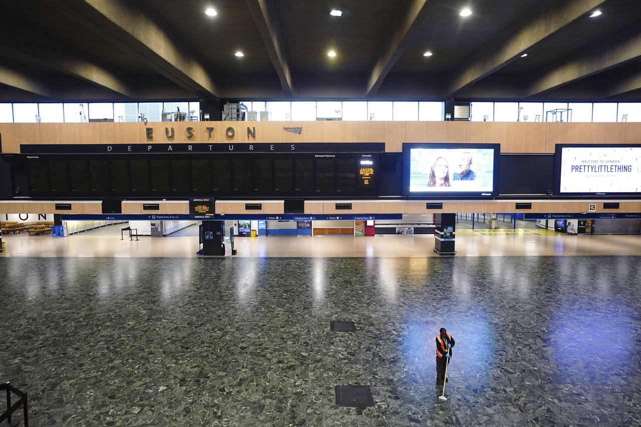A person sweeps the floor in front of an empty departures board at Euston station, as members of th...