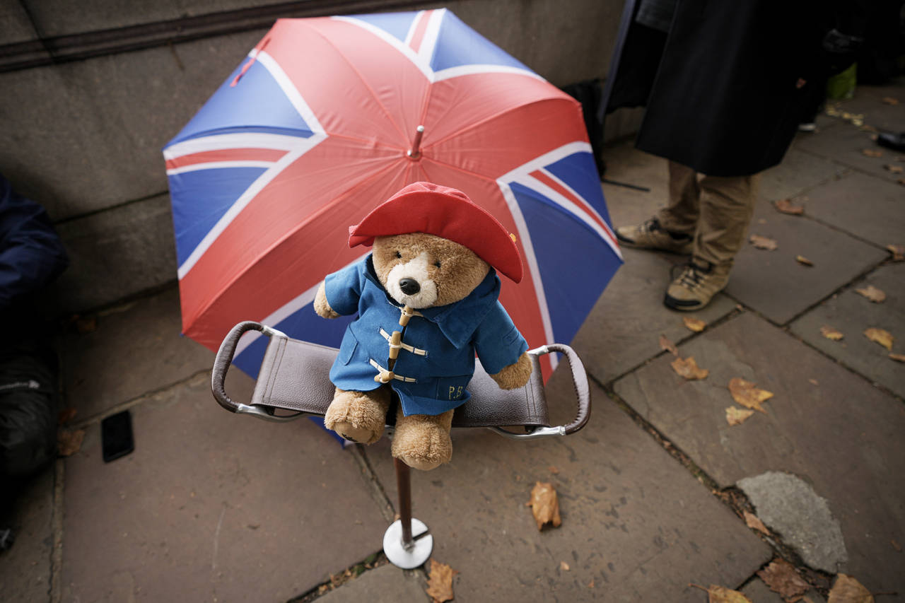 FILE - A Paddington bear stuffed toy is placed on a chair next to a Union flag umbrella as people w...
