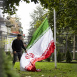 
              A protester takes down the Iranian flag on the ground of the Iranian embassy during the global protest against the Iranian regime in front of the Iranian embassy in Bern, Switzerland, Saturday, Oct. 1, 2022. They protest against the death of Mahsa Amini, a woman who died while in police custody in Iran. Mahsa Amini was arrested by Iran's morality police for allegedly violating its strictly-enforced dress code. (Peter Klaunzer/Keystone via AP)
            