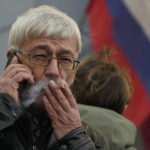 
              Oleg Orlov, a member of the Board of the International Historical Educational Charitable and Human Rights Society 'Memorial' (International Memorial) speaks by phone and smokes after a court hearing, with the Russian flag in the background, in Moscow, Russia, Friday, Oct. 7, 2022. On Friday, Oct. 7, 2022 the Nobel Peace Prize was awarded to jailed Belarus rights activist Ales Bialiatski, the Russian group Memorial and the Ukrainian organization Center for Civil Liberties. (AP Photo/Alexander Zemlianichenko)
            