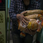 
              Volunteers distribute bread rations to civilians at a public school in Mykolaiv, Ukraine, Tuesday, Oct. 25, 2022. Mykolaiv residents pick up bread from the only food distribution point in Varvarivka, a Mykolaiv district where thousands of people live. One person is allowed to receive free bread just once in three days. (AP Photo/Emilio Morenatti)
            