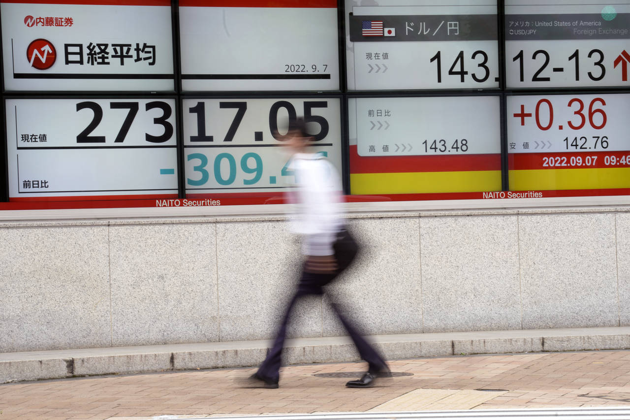 FILE - A person walks past an electronic stock board showing Japan's Nikkei 225 index and U.S. doll...