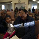
              Janet Kiyutelluk, 57, wipes her tears while singing a hymn as her granddaughter, Lacey Barr, 3, watches during a Sunday service at the Shishmaref Lutheran Church in Shishmaref, Alaska, Sunday, Oct. 2, 2022. (AP Photo/Jae C. Hong)
            