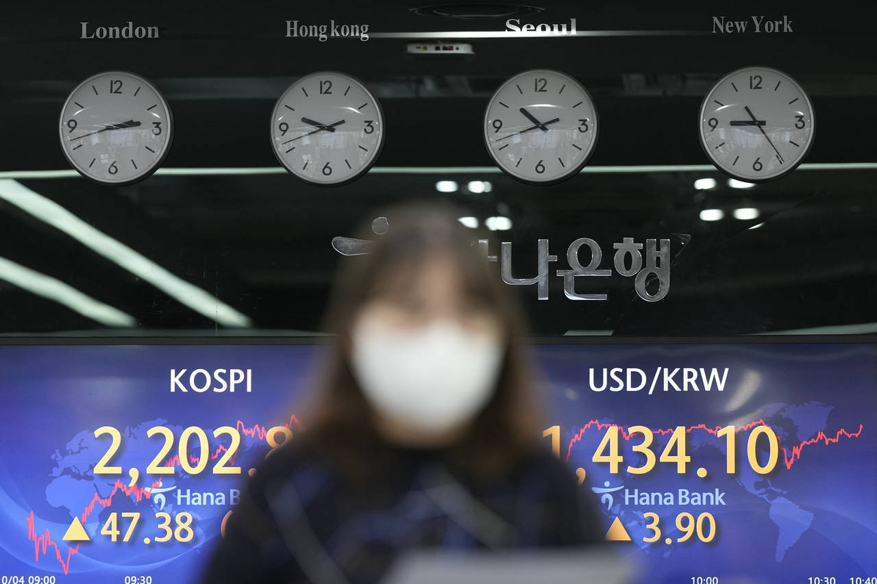 A currency trader walks by the screens showing the Korea Composite Stock Price Index (KOSPI), left,...