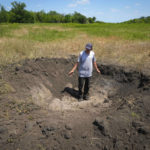
              FILE - A farmer stands in a crater left by a Russian shell on his field in the village of Ptyche in eastern Donetsk region, Ukraine, Sunday, June 12, 2022. (AP Photo/Efrem Lukatsky, File)
            