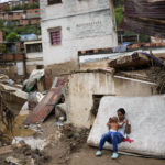 
              A woman holds a baby in front of her home damaged by flooding in Las Tejerias, Venezuela, Sunday, Oct. 9, 2022. At least 22 people died after intense rain caused flash floods and the overflow of a ravine, Vice President Delcy Rodríguez said. (AP Photo/Matias Delacroix)
            