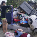 
              Alice Pujols goes through someone else's discarded items for clothes and shoes for her family Monday, Oct. 3, 2022, in Fort Myers, Fla. Pujols's home was completely destroyed after her home flooded due to rising waters caused by Hurricane Ian. (AP Photo/Marta Lavandier)
            