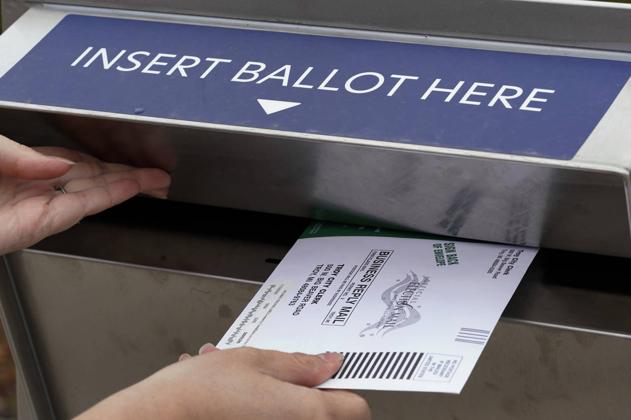 FILE - A Michigan voter inserts her absentee voter ballot into a drop box in Troy, Mich. on Oct. 15...