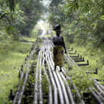 
              FILE- A woman walks along an oil pipeline in Warri, Nigeria, on Jan. 15, 2006. Nigerian state gas company has declared a force majeure after floods hindered gas operations, raising concerns among analysts about the West African nation's capacity to meet local and international demands. (AP Photo/George Osodi, File)
            