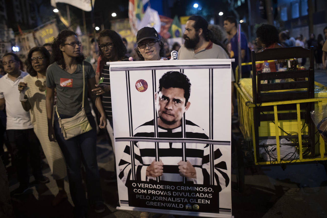 FILE - A woman holds a poster depicting Brazil's Justice Minister Sergio Moro behind bars, wearing ...