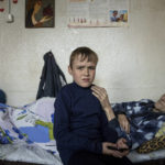 
              Mykola Svyryd, 70, touches the shoulder of his son Bohdan, in a shelter for injured and homeless people in Izium, Ukraine, Monday, Sept. 26, 2022. The young Ukrainian boy with disabilities, 13-year-old Bohdan, is now an orphan after his father, Mykola Svyryd, was taken by cancer in the devastated eastern city of Izium. (AP Photo/Evgeniy Maloletka)
            