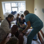 
              Dr. Yurii Kuznetsov, left, helps nurses to move a patient onto a bed at the hospital in Izium, Ukraine, Saturday, Sept. 17, 2022. Medical staff at the Izium hospital in eastern Ukraine are fighting the memories of six deadly months under Russian occupation. They also are looking darkly ahead at the coming months without electricity.  (AP Photo/Evgeniy Maloletka)
            