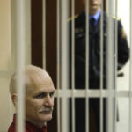 
              FILE- Ales Bialiatski, the jailed leader of Vesna, the most prominent human rights group in Belarus, sits in a cage during a court session in Minsk, Belarus, Thursday, Nov. 24, 2011. On Friday, Oct. 7, 2022 the Nobel Peace Prize was awarded to jailed Belarus rights activist Ales Bialiatski, the Russian group Memorial and the Ukrainian organization Center for Civil Liberties.  (AP Photo/Sergei Grits, File)
            