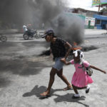 
              FILE - A woman guides a child past a demonstration against increasing violence in Port-au-Prince, Haiti, Tuesday, March 29, 2022. The protest coincides with the 35th anniversary of Haiti's 1987 constitution and follows other protests and strikes in recent weeks in the middle of a spike in gang-related kidnappings. (AP Photo/Odelyn Joseph, File)
            