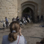 
              A spectator takes pictures as herders lead a bull into an arena bordering the medieval city walls of Aigues-Mortes during traditional festivities, Oct. 11, 2022. (AP Photo/Daniel Cole)
            